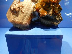 Англезит, Фосгенит. Огромные кристаллы фосгенита (слева, коричневато-бежевые со штриховкой) и англезита (желтоватые). Образец сфотографирован на Международной минералогической выставке в Мюнхене (Mineralientage München 2012).