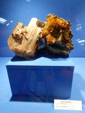 Англезит, Фосгенит. Огромные кристаллы фосгенита (слева, коричневато-бежевые со штриховкой) и англезита (желтоватые). Образец сфотографирован на Международной минералогической выставке в Мюнхене (Mineralientage München 2012).